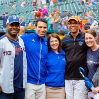 A group of the gvsu alumni staff and posing for a photo while standing on the infield of comerica park. There is also a camera man